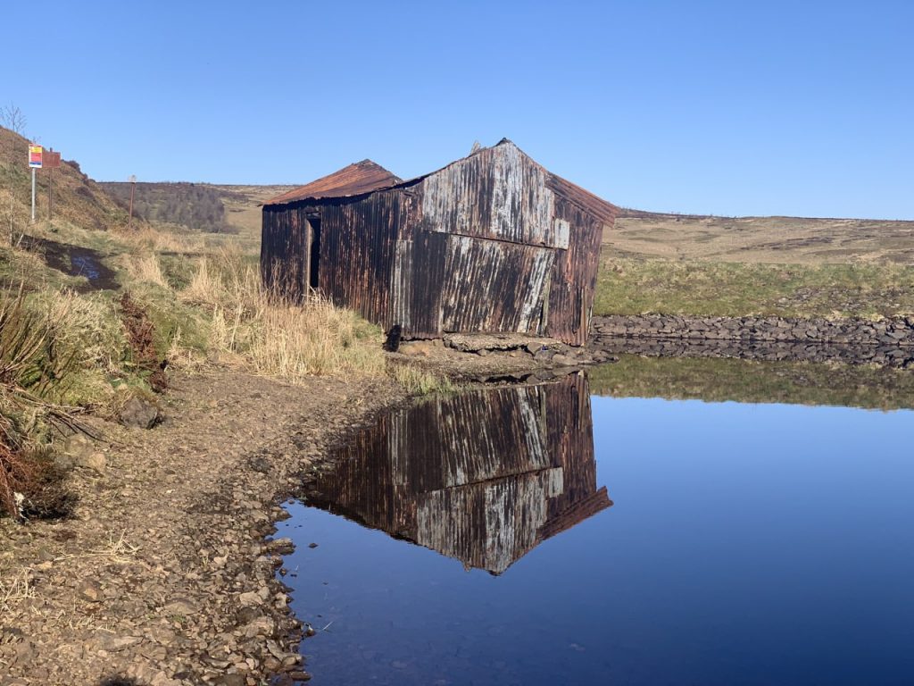 Corrugated iron hut reflected in loch 