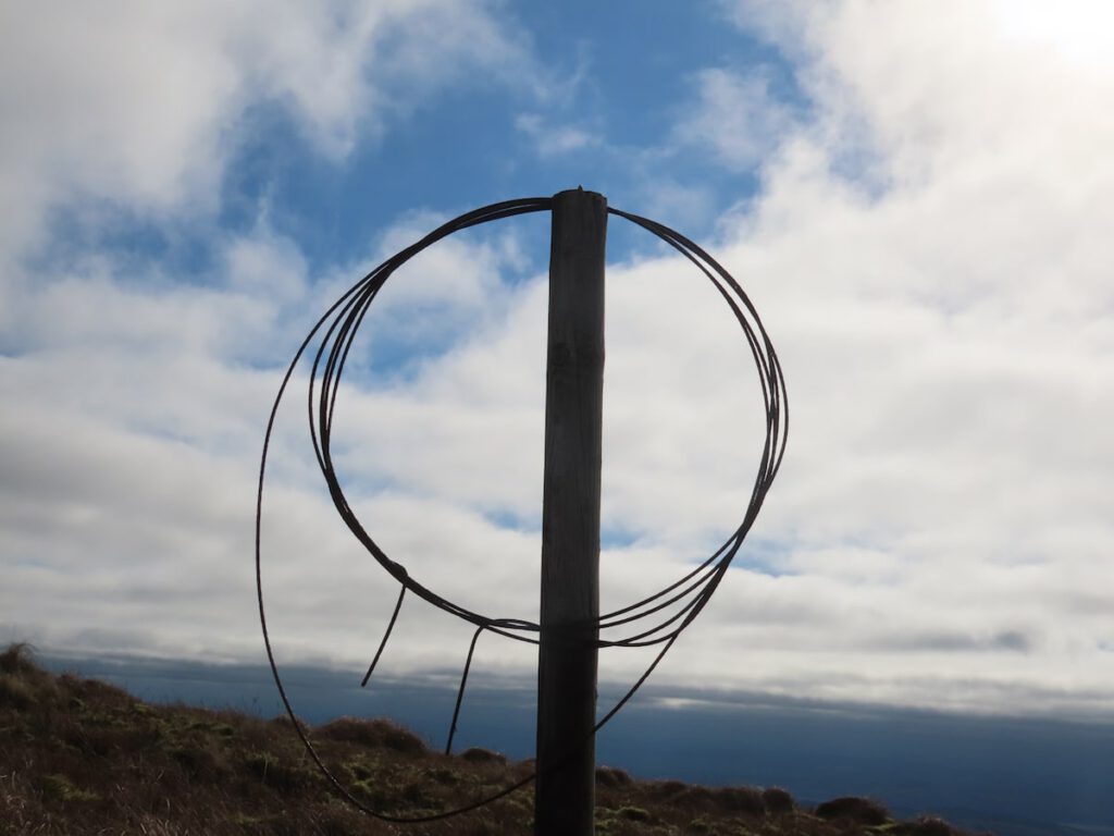 A fence post with a few loops of fence wire forming a circle hanging from the top of the post. The sky behind.
