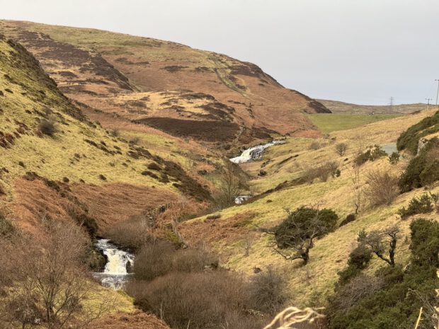 Loch Humphrey Burn. A burn with 2 visiable waterfalls flows down a small valley. It is winter, the ground is moslty old grass and heather. The colours brown & yellow.