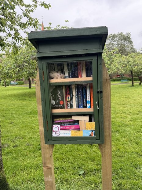 Small green outdoor library filled with books in a park.