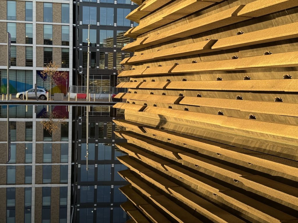 Side view of the V&A Dundee building with its layered, horizontal slabs reflected in water