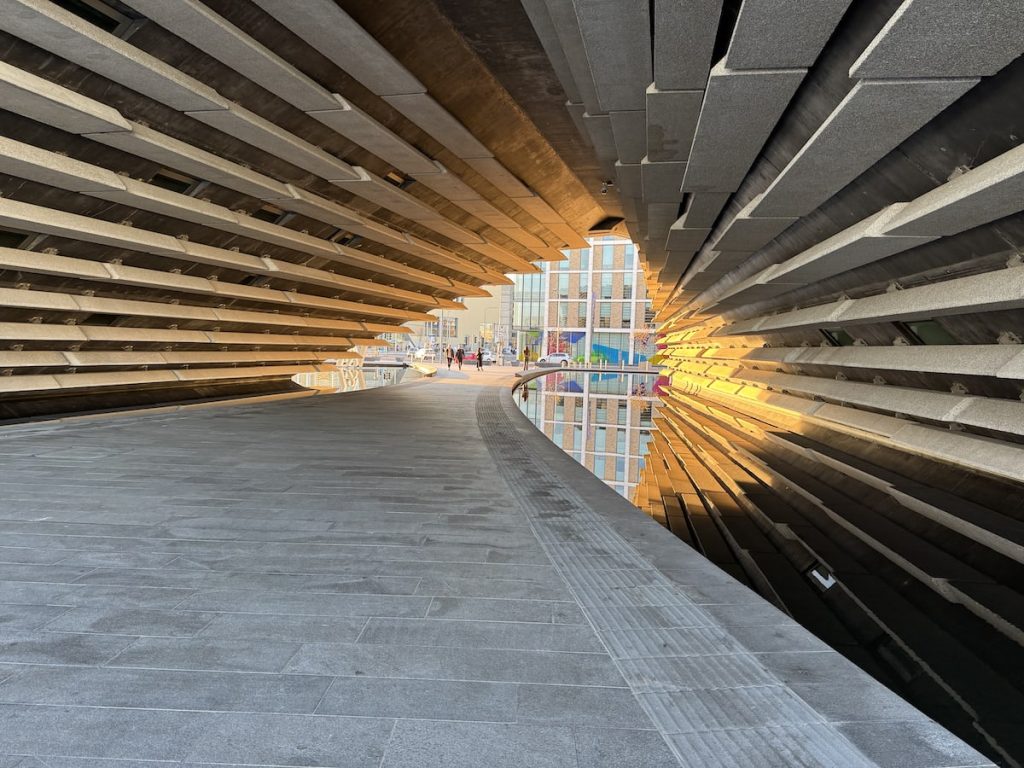 Interior view of a tunnel-like structure in the V&A Dundee building with layered panels and a reflecting pool.