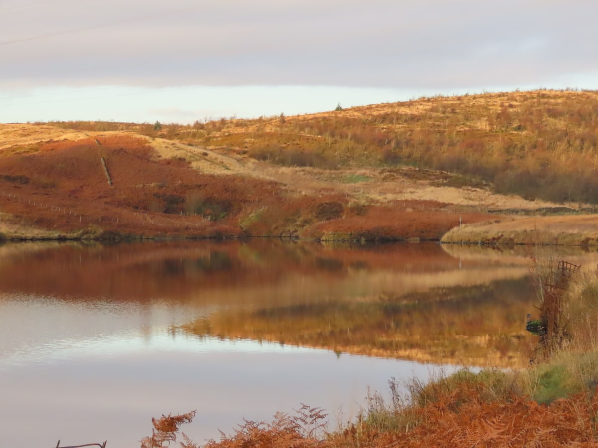 Tranquil landscape of Greenside Reservoir with reflections of autumnal hills.