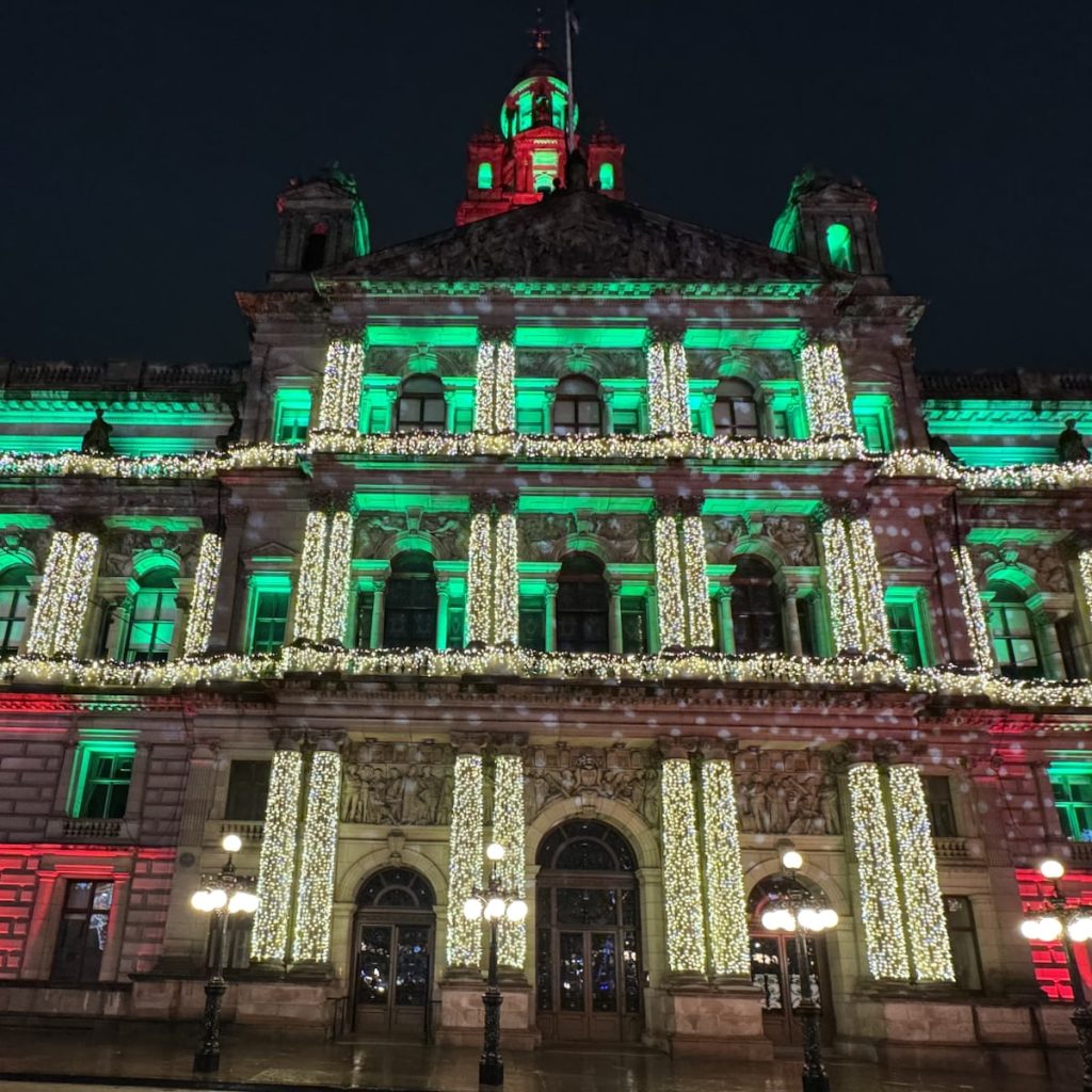 Glasgow City Hall illuminated with festive green, red, and white lights at night