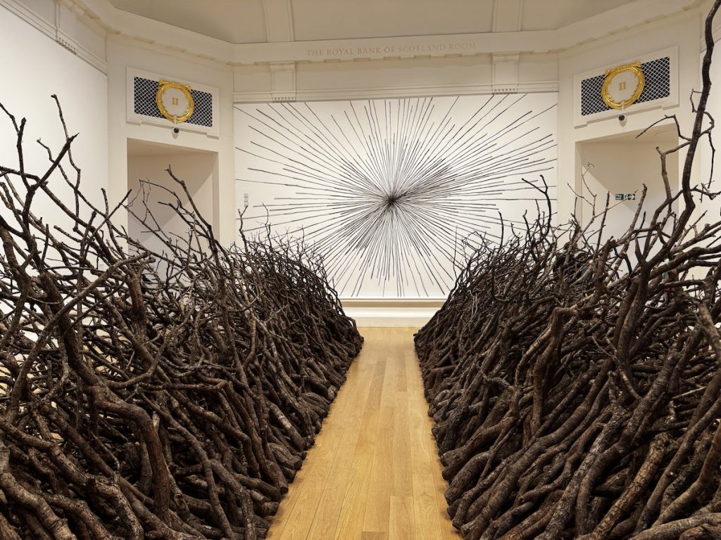 A passage between to walls of oak branches. A 'sun burst' of reeds at the end