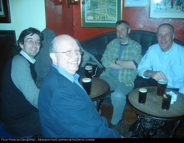 Four men sitting in a pub, smiling and talking, with pints of dark beer on two small tables. Bob, Ewan, Me & Will at the Jolly Judge.