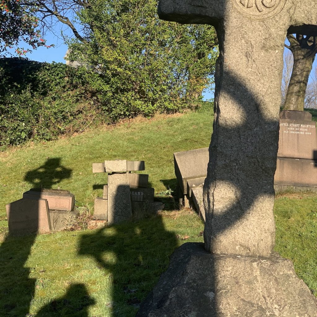 A graveyard with a large stone cross and several smaller tombstones on a grassy field.