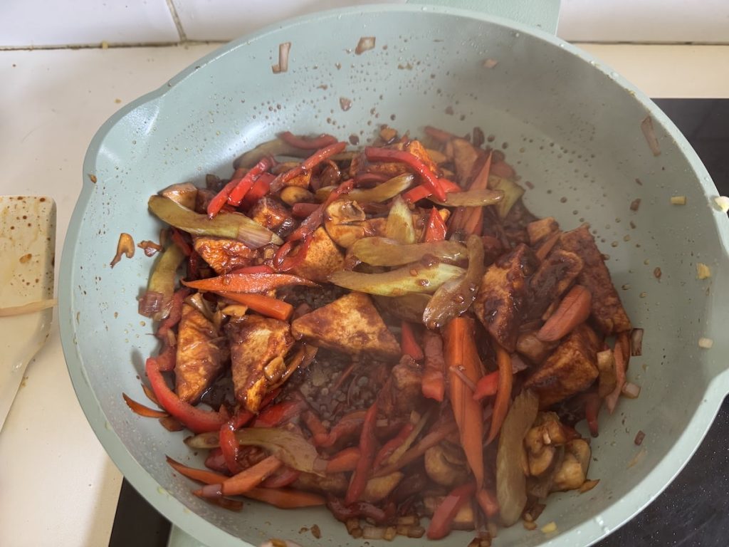 Frying pan with stir-fried tofu, bell peppers, onions, carrots, and mushrooms.